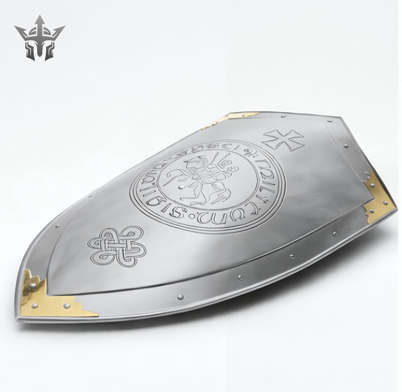 May include: A silver-colored shield with gold corner accents. The shield features an engraved emblem with a knight on horseback and a cross design. The shield has a pointed bottom and a curved top, with rivets along the edge.