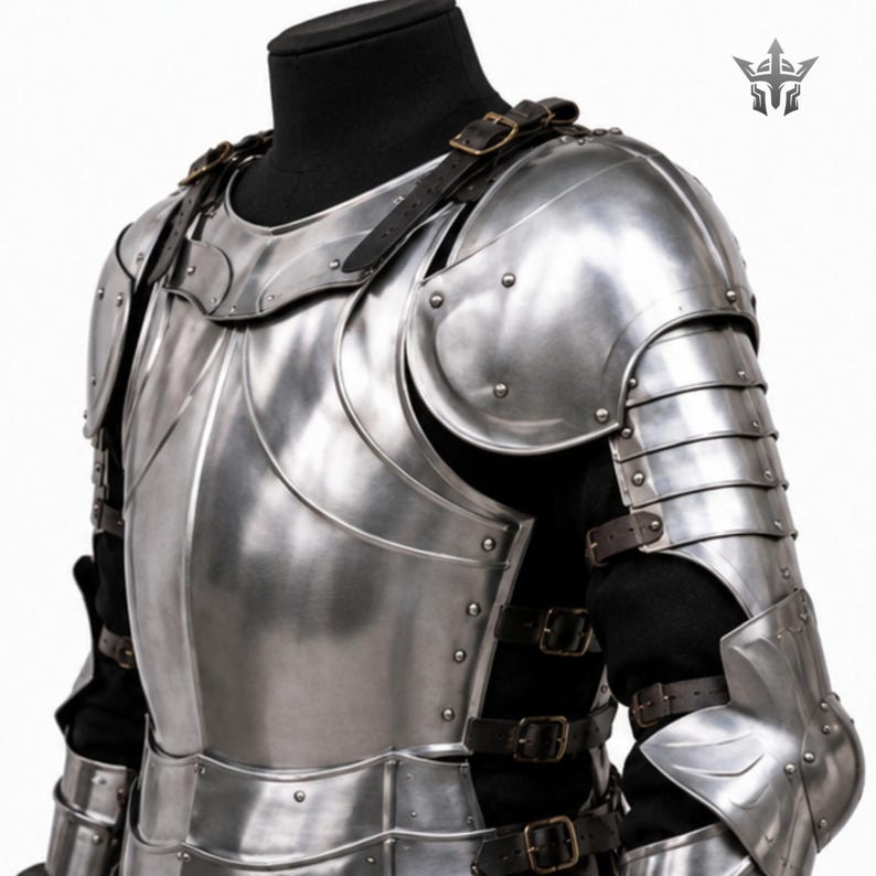 May include: A polished steel suit of armor featuring a breastplate, pauldrons, and articulated arm guards. The metal plates are secured with dark brown leather straps and brass-toned buckles over a black garment, with a logo in the top corner.