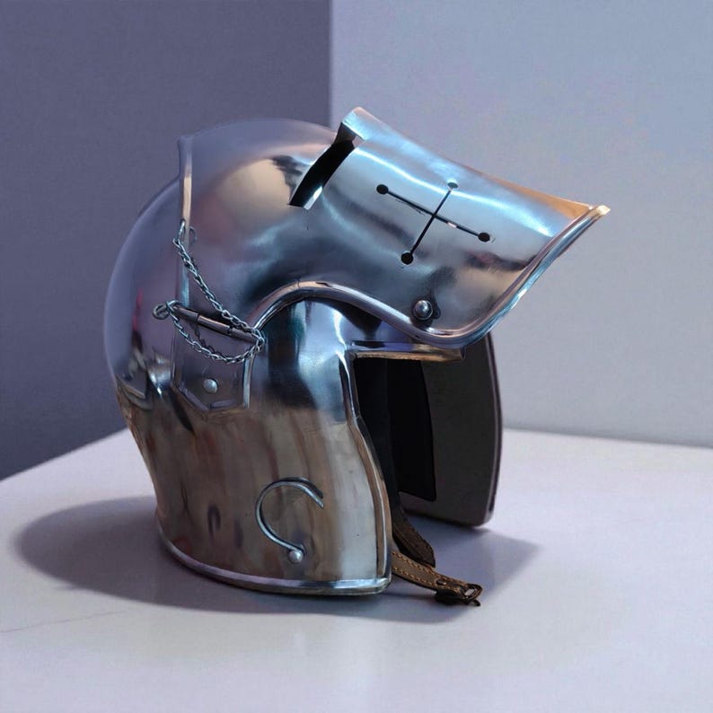 May include: A polished, silver-colored medieval helmet with a visor featuring a cross design. The helmet has a chain detail and a leather strap. The helmet is designed to protect the head and face.