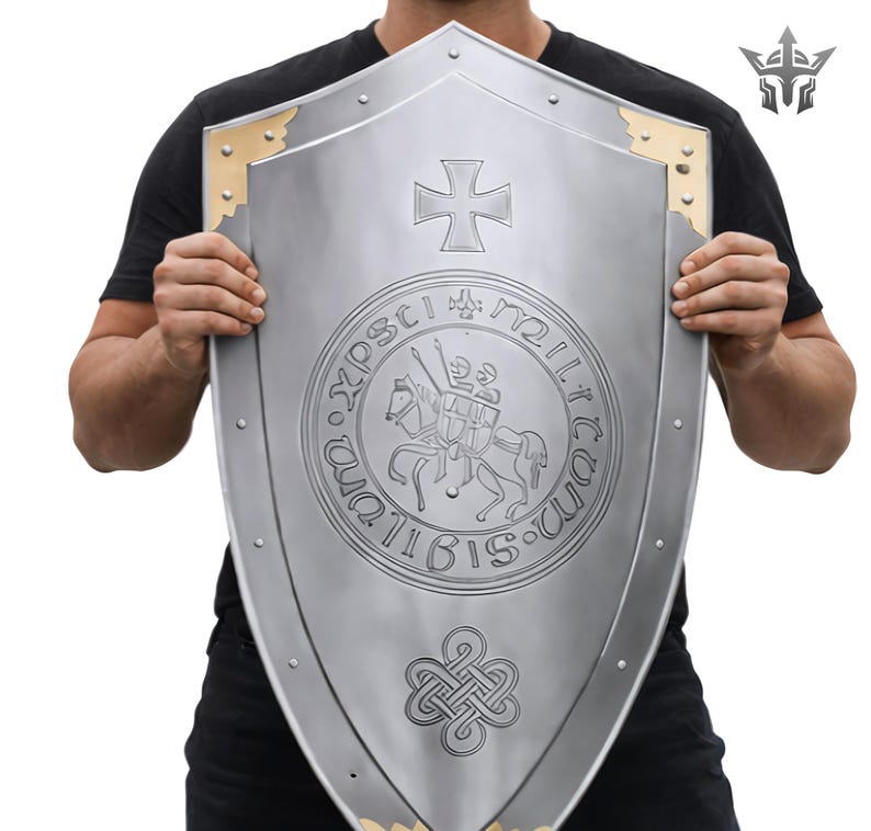 May include: A silver-colored shield with a cross emblem and a circular seal featuring a knight on horseback. The shield has gold-colored corner accents and rivet details, showcasing a medieval design.