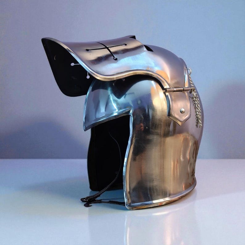 May include: A polished, silver-colored medieval helmet with a visor and a decorative chain. The helmet has a cross-shaped design on the visor and is made of reflective metal. The helmet is designed to protect the head and face.
