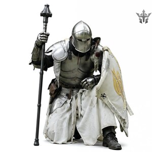 May include: A kneeling knight in full plate armor, holding a black staff and a shield. The shield features a gold emblem on a white background. The knight is wearing a silver helmet and black boots. The armor appears to be made of metal.