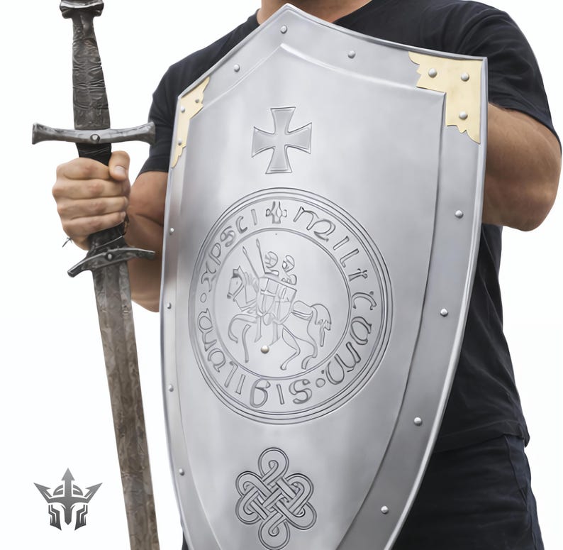 May include: A silver shield with a cross and a circular emblem, and a long sword. The shield has gold-colored corner accents and is held by a person wearing a black shirt. The sword is held in the other hand.