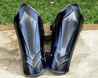 Peut inclure: Paire de protège-bras en métal noir avec une finition polie et réfléchissante. L'armure présente un design pointu sur le dessus et des arêtes décoratives. Une sangle en cuir noir avec boucles relie les deux pièces, thème médiéval ou fantastique.
