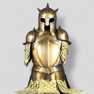 Op de afbeelding: Een goudkleurig harnas, met een helm met drie omhoog wijzende punten en ooggaten. Het harnas omvat schouderbeschermers en een borstplaat met ingewikkelde details. Het onderste deel heeft een geschubd ontwerp.