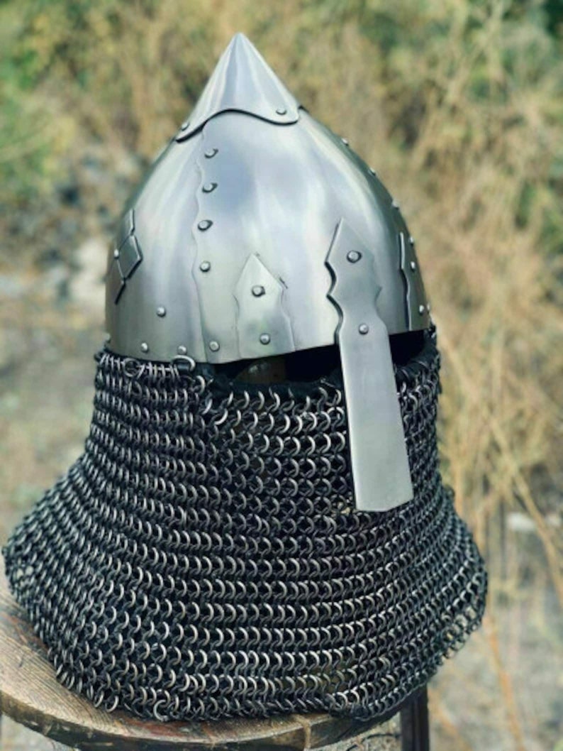May include: A medieval-style helmet with a pointed top and riveted construction. The helmet is made of shiny metal and features a chainmail neck guard. The design is reminiscent of historical armor.