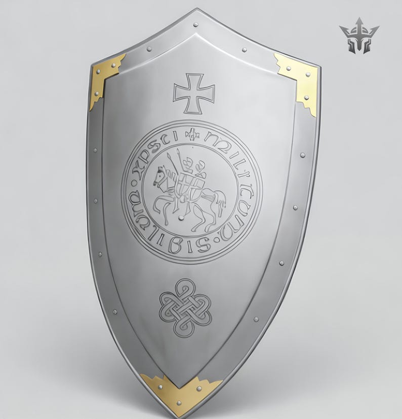May include: A silver-colored shield with a pointed bottom and rounded top. The shield features a cross at the top, a circular emblem with a knight on horseback, and gold-colored corner accents. The shield has a medieval theme.