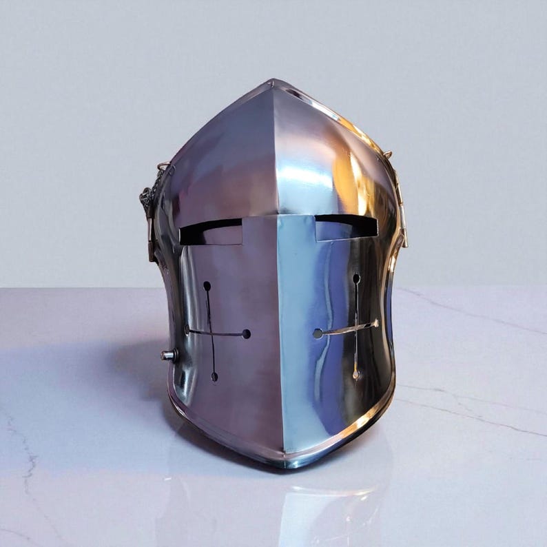 May include: A polished, silver-colored medieval helmet with a cross design on the front. The helmet has a smooth, reflective surface and a visor with eye slits. The helmet is designed to protect the head and face.