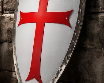 May include: A medieval shield with a white background and a large red cross. The shield has a metal border with rivets and is set against a rustic wooden and stone backdrop.