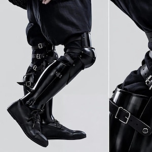 May include: Black leather leg armor with multiple buckle straps. The armor covers the knees and shins, paired with black shoes. The image is set against a plain background, highlighting the details of the protective gear.