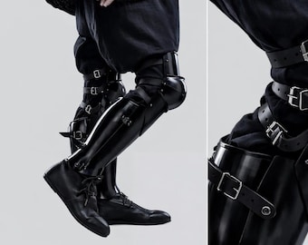 May include: Black leather leg armour with multiple buckle straps. The armour covers the knees and shins, paired with black shoes. The image is set against a plain background, highlighting the details of the protective gear.