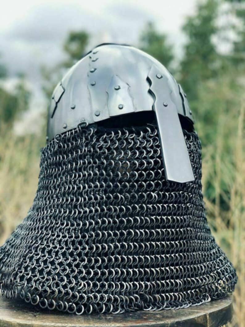 May include: A medieval-style helmet with a riveted, polished metal skullcap and a chainmail aventail. The helmet features a rectangular visor and is designed for protection. The chainmail extends to cover the neck and shoulders.