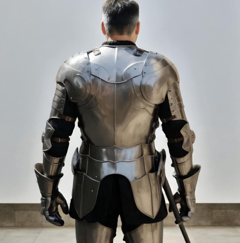 May include: A polished steel suit of armor featuring a breastplate, pauldrons, articulated arm guards, and gauntlets. The metallic plates are secured with brown leather straps over a black garment, covering the torso, shoulders, and arms.