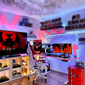 Puede incluir: Una configuración de juego con una silla de juego blanca y roja, un escritorio blanco con un teclado de juego rojo y blanco, un ratón de juego rojo y blanco, un monitor negro con un logotipo de juego rojo y blanco y unos auriculares de juego rojos y blancos. La habitación está decorada con un techo en forma de nube, una pared blanca con un patrón geométrico y una estantería blanca con una colección de figuras.