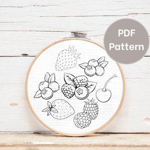Puede incluir: Patrón de bordado en blanco y negro de diferentes bayas, incluyendo fresas, frambuesas y arándanos. El patrón se muestra en un aro de bordado redondo sobre un fondo de madera blanco. El texto "PDF Pattern" se muestra en un círculo gris.