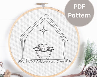 May include: Black and white line drawing of a baby Jesus in a manger with a star above. The image is in a round embroidery hoop.