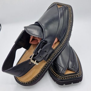 May include: A pair of black leather sandals with a buckle fastening and decorative stitching around the sole.