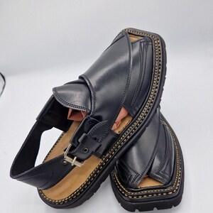 May include: A pair of black leather sandals with a buckle fastening and decorative stitching around the sole.
