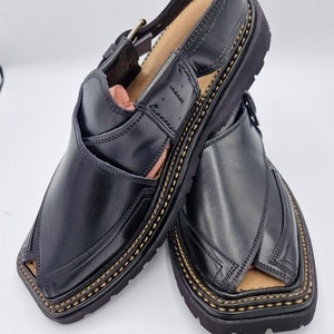 May include: A pair of black leather sandals with a closed toe and an open heel. The sandals have a thick, black sole with a gold stitching detail. The sandals have a buckle closure on the ankle strap.