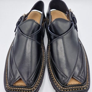 May include: A pair of black leather sandals with a buckle fastening and decorative stitching around the edge. The sandals have a pointed toe and a flat sole.