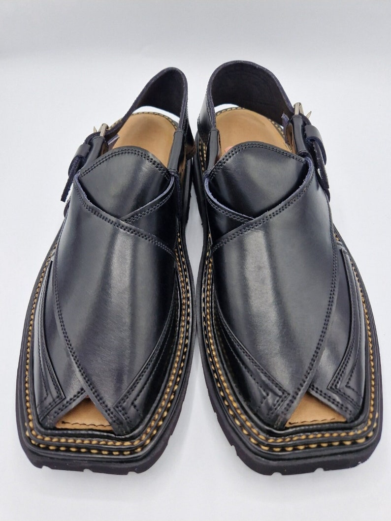 May include: A pair of black leather sandals with a buckle fastening and decorative stitching around the edge. The sandals have a pointed toe and a flat sole.