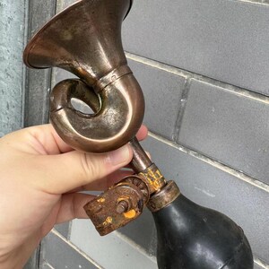 Puede incluir: Una bocina de bicicleta antigua de lat&oacute;n con una pera de goma negra. La bocina tiene un dise&ntilde;o curvo y una campana acampanada. El metal muestra signos de edad y desgaste, con un aspecto oxidado en algunas partes.