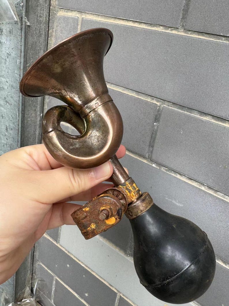 Puede incluir: Una bocina de bicicleta antigua de lat&oacute;n con una pera de goma negra. La bocina tiene un dise&ntilde;o curvo y una campana acampanada. El metal muestra signos de edad y desgaste, con un aspecto oxidado en algunas partes.