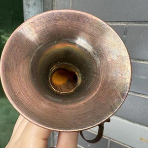 Puede incluir: Objeto en forma de embudo de color cobre con una abertura circular. El interior tiene un tono dorado y el exterior muestra signos de desgaste. Un peque&ntilde;o asa curvada es visible en el lateral. El objeto parece ser un art&iacute;culo vintage o antiguo.