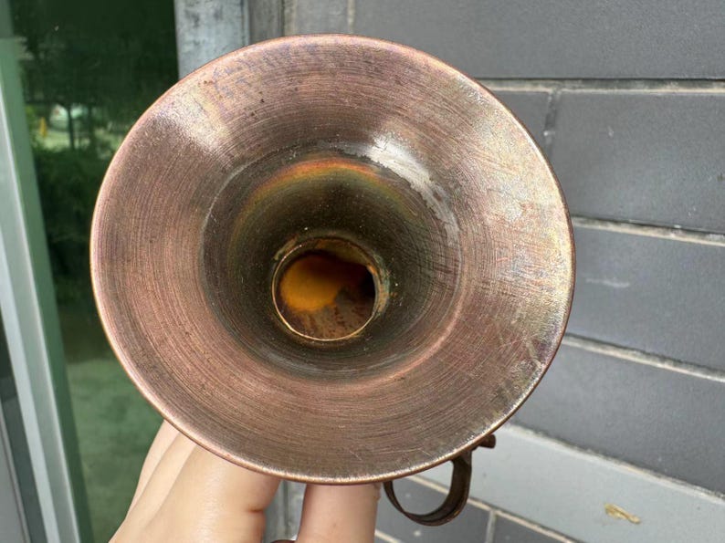 Puede incluir: Objeto en forma de embudo de color cobre con una abertura circular. El interior tiene un tono dorado y el exterior muestra signos de desgaste. Un peque&ntilde;o asa curvada es visible en el lateral. El objeto parece ser un art&iacute;culo vintage o antiguo.