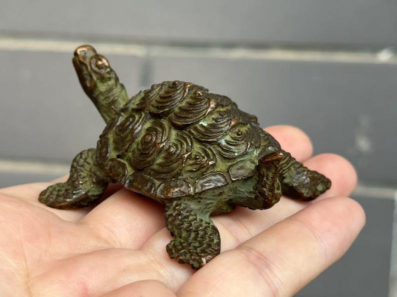 May include: A detailed bronze turtle figurine with a textured shell and detailed legs and head. The turtle is a dark green color with bronze highlights. The figurine is approximately 4 inches long.