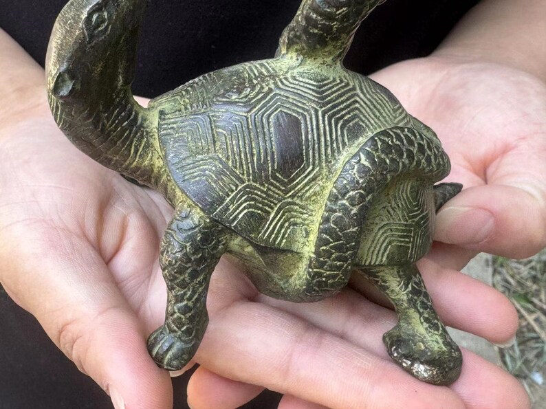 May include: A bronze turtle figurine with a detailed shell pattern and textured skin. The sculpture has a weathered, antique appearance, with green and brown tones. The turtle is depicted in a crawling position, showcasing its legs and head.