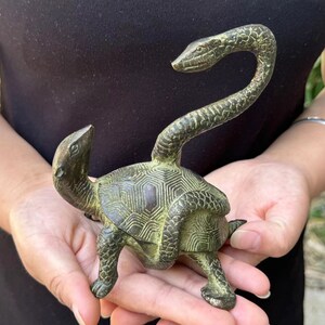 May include: Bronze sculpture of a turtle with a snake's head and neck extending upwards. The turtle has a detailed shell pattern and is in a walking pose. The sculpture has a weathered, antique appearance.