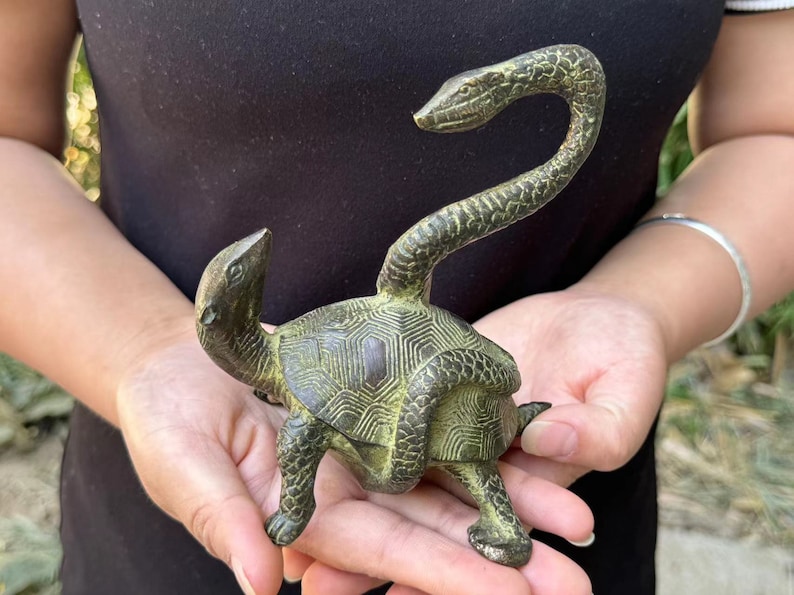 May include: Bronze sculpture of a turtle with a snake's head and neck extending upwards. The turtle has a detailed shell pattern and is in a walking pose. The sculpture has a weathered, antique appearance.
