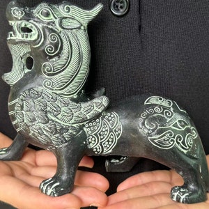 Könnte beinhalten: Eine kleine, kunstvoll geschnitzte Bronzestatue in Grün und Weiß, die eine mythische Kreatur mit Flügeln und einem langen Schwanz darstellt. Die Kreatur hat einen grimmigen Ausdruck und steht auf allen Vieren.