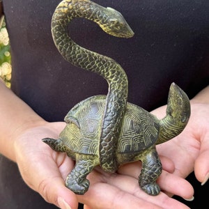 May include: Bronze sculpture of a turtle with a snake wrapped around it. The turtle has a detailed shell pattern, and the snake is coiled around the turtle's body. The sculpture has a weathered, antique appearance.