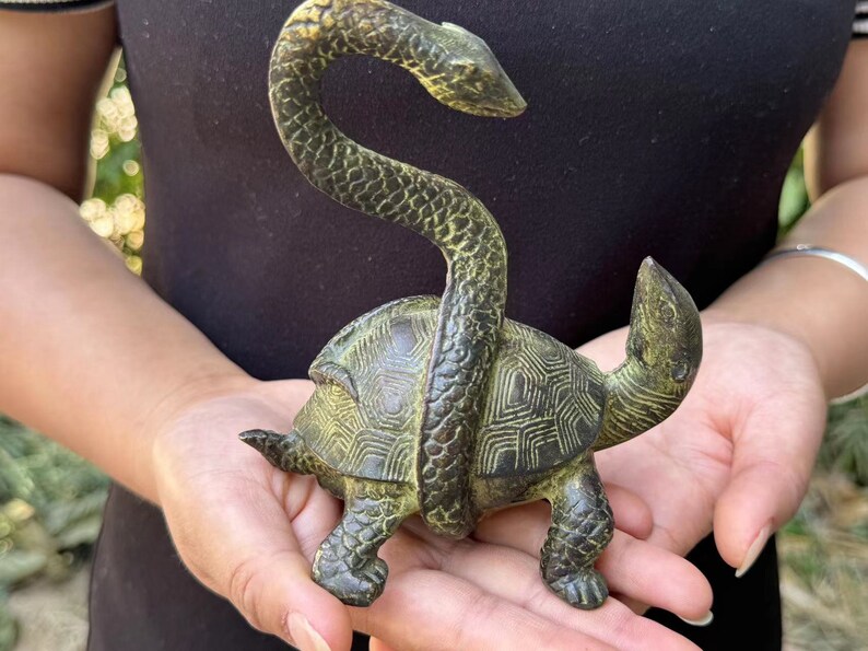 May include: Bronze sculpture of a turtle with a snake wrapped around it. The turtle has a detailed shell pattern, and the snake is coiled around the turtle's body. The sculpture has a weathered, antique appearance.