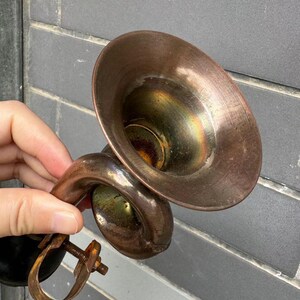 Puede incluir: Auricular de tel&eacute;fono antiguo de color cobre. El auricular tiene un receptor acampanado en forma de cono y un asa curvada. El metal muestra signos de edad y desgaste, con una p&aacute;tina deslustrada. El dise&ntilde;o recuerda la tecnolog&iacute;a de comunicaci&oacute;n de principios del siglo XX.