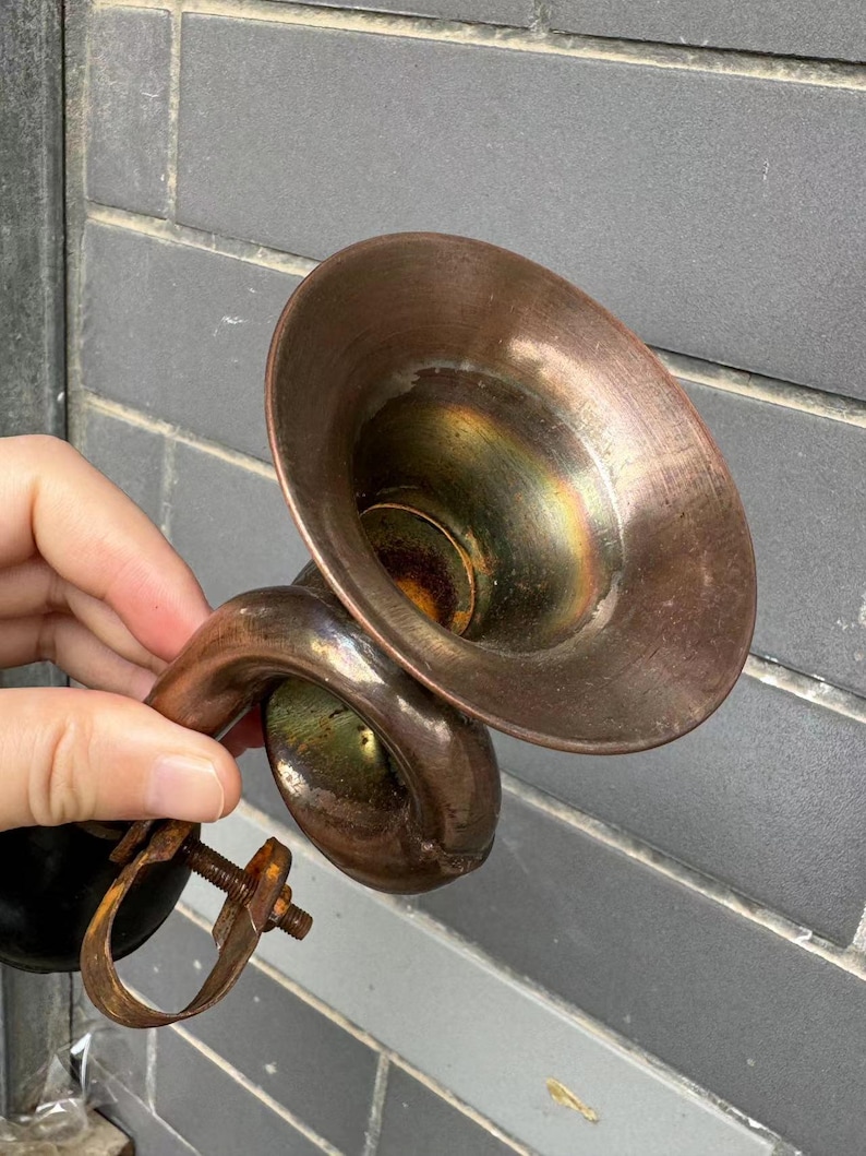 Puede incluir: Auricular de tel&eacute;fono antiguo de color cobre. El auricular tiene un receptor acampanado en forma de cono y un asa curvada. El metal muestra signos de edad y desgaste, con una p&aacute;tina deslustrada. El dise&ntilde;o recuerda la tecnolog&iacute;a de comunicaci&oacute;n de principios del siglo XX.