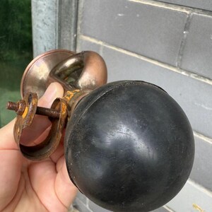 Puede incluir: Una bocina antigua de lat&oacute;n y cobre con una pera de goma negra. La bocina tiene un dise&ntilde;o curvo y se sostiene en una mano. Los componentes met&aacute;licos muestran signos de edad y desgaste, con un aspecto oxidado.