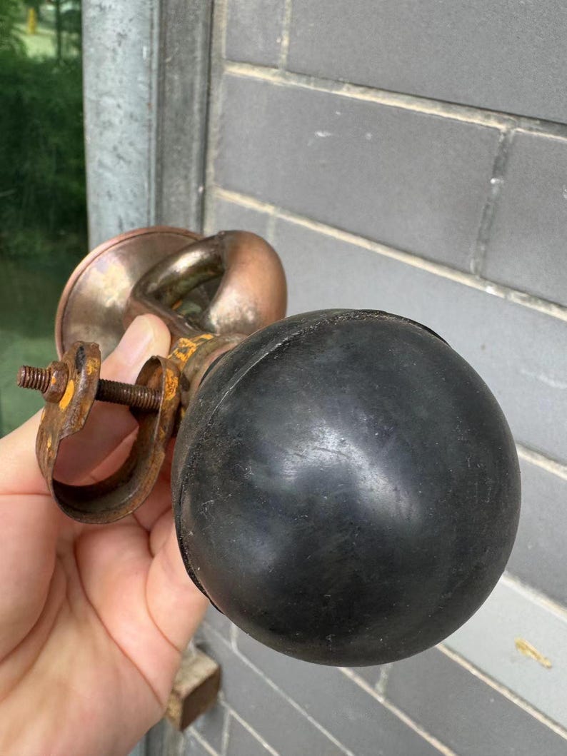 Puede incluir: Una bocina antigua de lat&oacute;n y cobre con una pera de goma negra. La bocina tiene un dise&ntilde;o curvo y se sostiene en una mano. Los componentes met&aacute;licos muestran signos de edad y desgaste, con un aspecto oxidado.