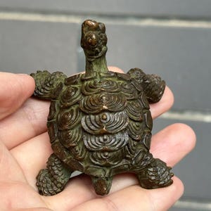May include: A bronze turtle figurine with detailed shell patterns and textured skin. The turtle has its head and legs extended, giving it a lifelike appearance. The figurine is a decorative item.