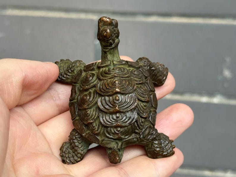 May include: A bronze turtle figurine with detailed shell patterns and textured skin. The turtle has its head and legs extended, giving it a lifelike appearance. The figurine is a decorative item.
