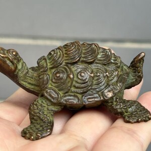 May include: A bronze-colored turtle figurine with detailed shell and textured skin. The sculpture is small, with its head and legs extended. The turtle is a decorative item, possibly for a desk or shelf.