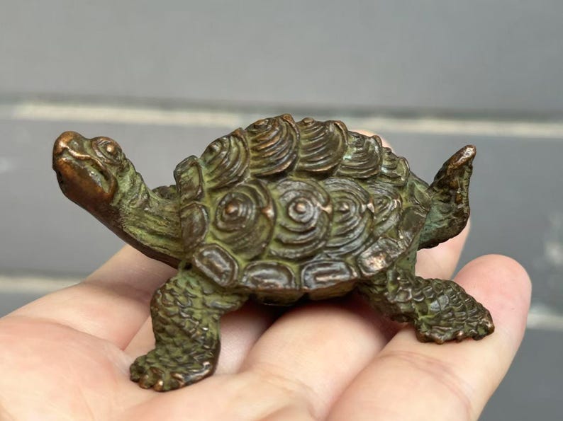 May include: A bronze-colored turtle figurine with detailed shell and textured skin. The sculpture is small, with its head and legs extended. The turtle is a decorative item, possibly for a desk or shelf.