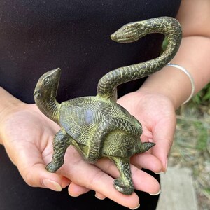 May include: A bronze sculpture of a turtle with a snake rising from its back. The turtle has a detailed shell pattern. The snake's head is raised, and the sculpture has a weathered, antique appearance.