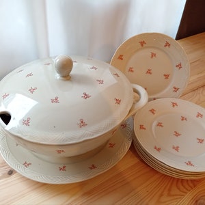 Könnte beinhalten: Eine weiße Suppenterrine aus Keramik mit Deckel und Blumenmuster. Die Terrine steht auf einem passenden Teller. Es gibt auch vier kleinere Teller mit dem gleichen Blumenmuster.