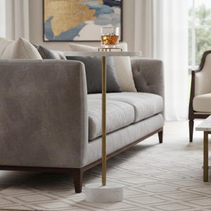 A round marble table with a gold metal base. The table is white with gray veining and the base is a cylinder shape.