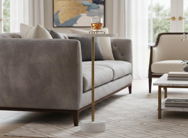 A round marble table with a gold metal base. The table is white with gray veining and the base is a cylinder shape.
