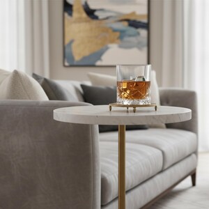 A round marble table with a gold metal base. The table is white with gray veining and the base is a cylinder shape.