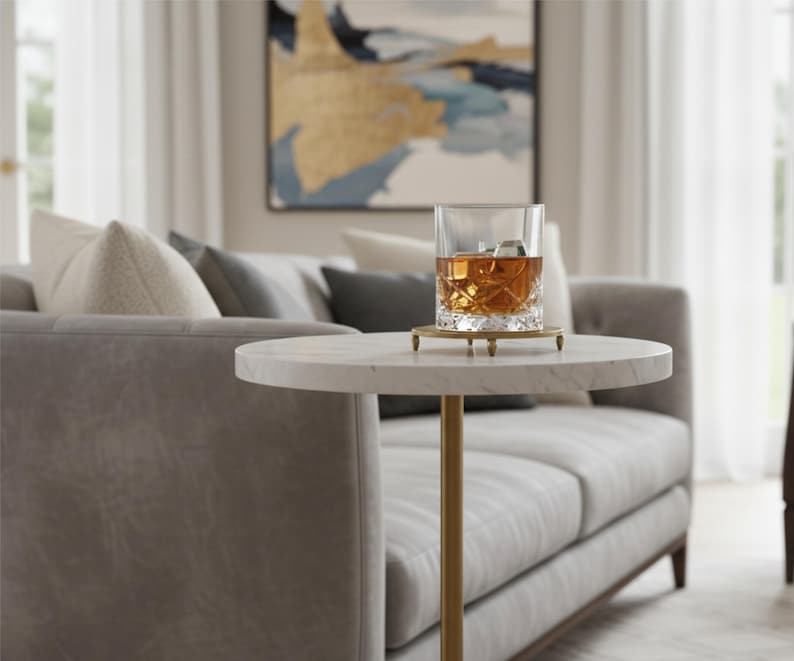 A round marble table with a gold metal base. The table is white with gray veining and the base is a cylinder shape.